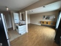 Open-concept living area featuring wood-finish flooring, track lighting, and a kitchen with tile flooring and white appliances - 306 11340 124, Edmonton, AB 