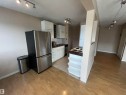 Open-concept kitchen featuring wood-finish flooring, white cabinetry, a built-in range, and a breakfast bar with open shelving - 306 11340 124, Edmonton, AB 