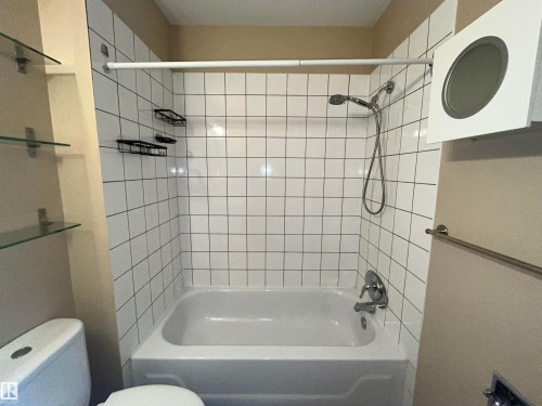 Bathroom featuring a white subway tile surround bathtub with a chrome shower fixture, a recessed lighting fixture, and glass shelving units - 306 11340 124, Edmonton, AB 