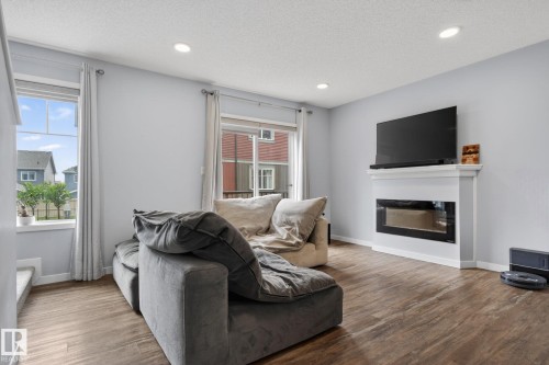 Living area featuring wood-finish flooring, recessed lighting, and a modern fireplace with a white mantel - 62 3305 Orchards Link, Edmonton, AB 