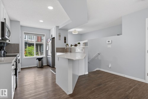 Kitchen featuring a multi-level island with a light-toned countertop, stainless steel appliances, wood-finish flooring, and recessed ceiling lighting - 62 3305 Orchards Link, Edmonton, AB 