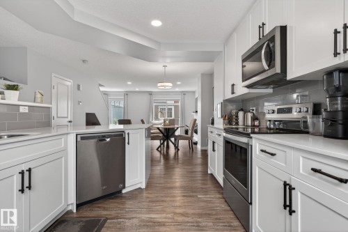 Well-appointed kitchen featuring white cabinetry, stainless steel appliances, light-toned countertops, and a gray subway tile backsplash - 62 3305 Orchards Link, Edmonton, AB 