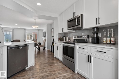 Contemporary kitchen featuring white shaker cabinetry, stainless steel appliances, a light-toned countertop, and a gray subway tile backsplash - 62 3305 Orchards Link, Edmonton, AB 