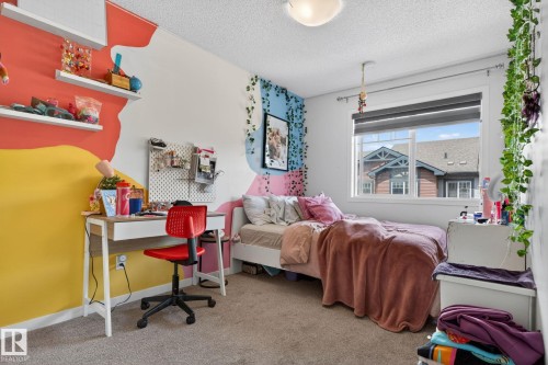 Bedroom featuring a window with blinds, a light fixture, carpeted flooring, and a wall-mounted desk - 62 3305 Orchards Link, Edmonton, AB 