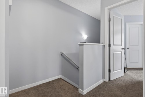Carpeted hallway featuring light gray walls, white trim, and a white paneled door - 62 3305 Orchards Link, Edmonton, AB 