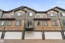 Modern multi-level townhome featuring a mix of horizontal siding and vertical paneling, an integrated single-car garage, a second-story balcony with metal railing, and multiple windows with dark trim - 62 3305 Orchards Link, Edmonton, AB 