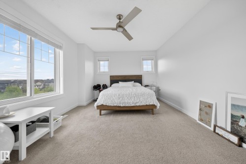 Bright room featuring a large window with multiple panes, two smaller windows, a ceiling fan with integrated lighting, and neutral-toned carpeting - 5 903 Crystallina Nera Way, Edmonton, AB 