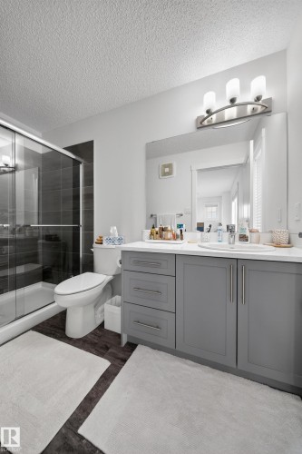 Bathroom featuring a glass-enclosed shower with dark tile surround, a white toilet, and dark wood-finish flooring - 5 903 Crystallina Nera Way, Edmonton, AB 