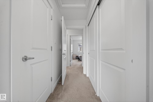 Hallway featuring white paneled doors, brushed nickel hardware, and a neutral carpeted floor - 5 903 Crystallina Nera Way, Edmonton, AB 