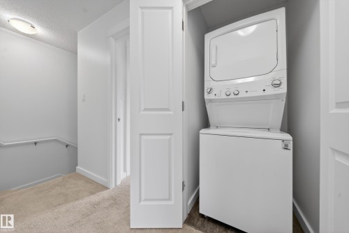 Space-saving stacked washer and dryer unit, paneled interior doors, light-toned carpeting, and a ceiling-mounted light fixture - 5 903 Crystallina Nera Way, Edmonton, AB 
