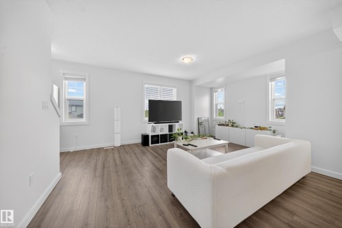 Bright living space featuring wood-finish flooring, white walls, and multiple windows - 5 903 Crystallina Nera Way, Edmonton, AB 