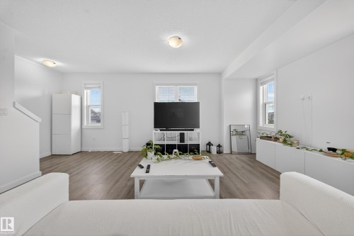 Spacious living area featuring wood-finish flooring, ample natural light from multiple windows, and recessed ceiling lighting - 5 903 Crystallina Nera Way, Edmonton, AB 