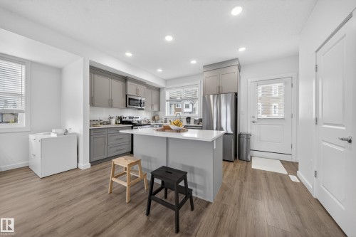 Open-concept kitchen featuring an island with a quartz countertop, stainless steel appliances, two-tone cabinetry, wood-finish flooring, and recessed lighting - 5 903 Crystallina Nera Way, Edmonton, AB 
