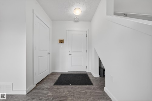 Entryway featuring a solid panel door, wood-finish flooring, white baseboards, and a flush mount ceiling light - 5 903 Crystallina Nera Way, Edmonton, AB 