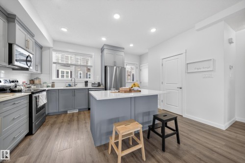Modern kitchen featuring grey shaker-style cabinetry, stainless steel appliances, white subway tile backsplash, and a central island with a white countertop - 5 903 Crystallina Nera Way, Edmonton, AB 