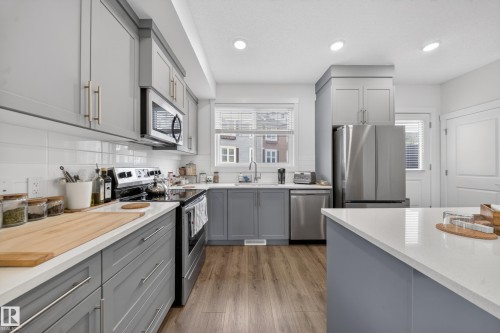 Modern kitchen featuring gray cabinetry, white countertops, stainless steel appliances, and wood-finish flooring - 5 903 Crystallina Nera Way, Edmonton, AB 