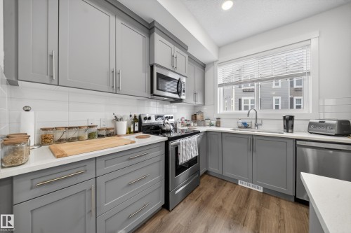 Kitchen featuring light gray shaker-style cabinetry, white subway tile backsplash, white countertops, wood-finish flooring, and stainless steel appliances - 5 903 Crystallina Nera Way, Edmonton, AB 