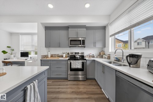 Modern kitchen featuring grey shaker-style cabinetry, stainless steel appliances, white subway tile backsplash, and wood-finish flooring - 5 903 Crystallina Nera Way, Edmonton, AB 