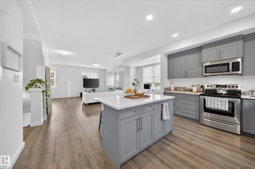 Open-concept kitchen featuring gray cabinetry, stainless steel appliances, a white subway tile backsplash, and a central island with a white countertop - 5 903 Crystallina Nera Way, Edmonton, AB 