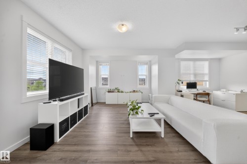 Open-concept living space featuring wood-finish flooring and multiple windows with blinds - 5 903 Crystallina Nera Way, Edmonton, AB 
