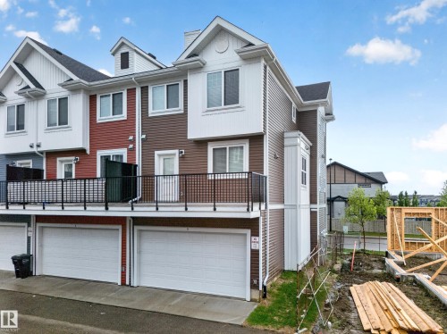 Multi-level townhome featuring a brown and white exterior, white garage doors, a black balcony railing, and multiple windows - 5 903 Crystallina Nera Way, Edmonton, AB 