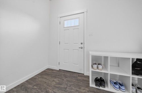 Entryway featuring wood-finish flooring, white baseboards, a white paneled door with glass inserts, and a chrome door handle - 5 903 Crystallina Nera Way, Edmonton, AB 