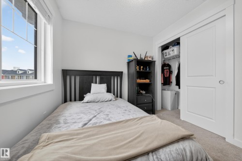 Bedroom featuring a large window, white trim, light-toned carpeting, and a closet with sliding panel doors - 5 903 Crystallina Nera Way, Edmonton, AB 