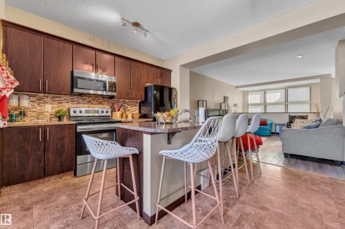 Kitchen featuring dark wood-finish cabinetry, stainless steel appliances, and a mosaic tile backsplash - 621 Mcdonough Link Link, Edmonton, AB 