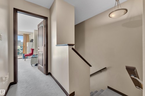 Carpeted hallway and staircase featuring dark wood trim, banister, and handrail - 621 Mcdonough Link Link, Edmonton, AB 