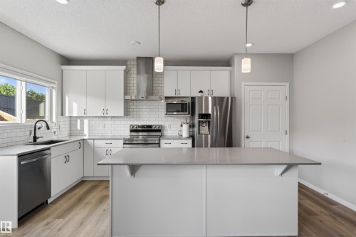 Contemporary kitchen featuring white cabinetry, subway tile backsplash, stainless steel appliances, a center island with countertop seating, and wood-finish flooring - 22638 99A Avenue, Edmonton, AB 