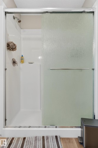 Shower enclosure featuring a sliding privacy glass door with a polished chrome handle, white multi-piece shower surround, and brushed nickel showerhead with coordinated fixtures - 22638 99A Avenue, Edmonton, AB 
