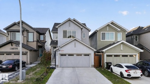 Modern multi-story home featuring light gray vertical and horizontal siding, a two-car garage with a concrete driveway, and a gabled roofline - 22638 99A Avenue, Edmonton, AB 