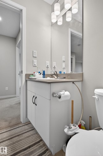 Bathroom vanity featuring white cabinetry with dark hardware, a light-toned countertop, and an integrated sink with a chrome faucet - 22638 99A Avenue, Edmonton, AB 