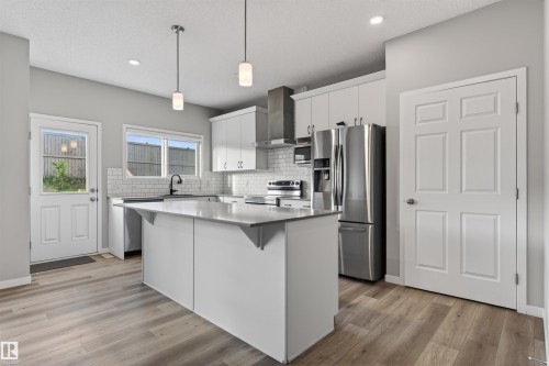Modern kitchen featuring a central island with a light-toned countertop, white cabinetry, and stainless steel appliances - 22638 99A Avenue, Edmonton, AB 