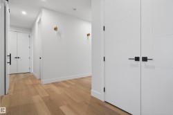 Hallway featuring light wood-finish flooring, white walls, recessed ceiling lighting, and modern white doors with black hardware - 