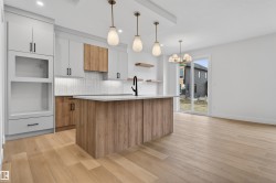 Modern kitchen featuring a large central island, light wood-finish flooring, white upper cabinetry, and a textured tile backsplash - 
