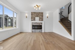 Spacious living area featuring light wood-finish flooring, a stone-clad fireplace with a white mantel, and large windows - 