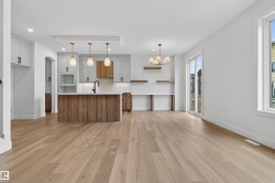 Kitchen and dining area featuring wood-finish flooring, a central island with integrated sink, pendant lighting, sliding glass doors, and a chandelier - 