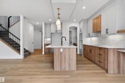 Contemporary kitchen featuring a large island with sink, two-tone cabinetry, light wood-finish flooring, and a subway tile backsplash - 