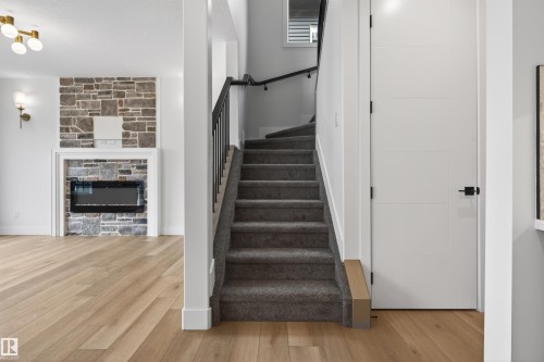 Carpeted staircase with black wrought iron railing, complemented by wood-finish flooring and a stone-accented fireplace with an electric insert - 15 Redbud Way, St. Albert, AB - Indoor Photo Showing Other Room