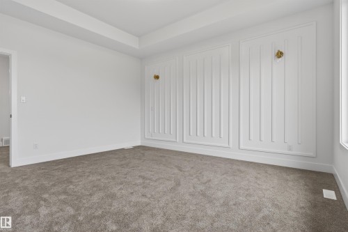 Spacious room featuring textured carpet flooring, bright white walls, and decorative wall paneling with integrated sconce lighting - 15 Redbud Way, St. Albert, AB - Indoor Photo Showing Other Room