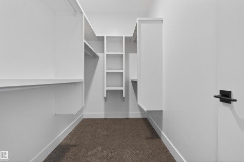 Spacious walk-in closet featuring white built-in shelving, hanging rods, and a neutral-toned carpet flooring - 15 Redbud Way, St. Albert, AB - Indoor With Storage