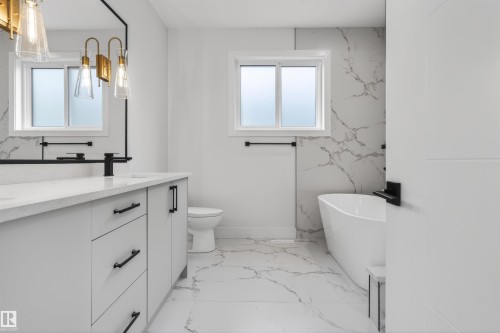 Bathroom featuring a double vanity with matte black hardware, a freestanding soaking tub, and large format marble-look tile flooring - 15 Redbud Way, St. Albert, AB - Indoor Photo Showing Bathroom