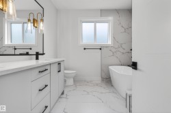 Bathroom featuring a double vanity with matte black hardware, a freestanding soaking tub, and large format marble-look tile flooring - 