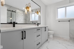 Bathroom featuring a double vanity with light gray cabinetry, matte black hardware, and an expansive mirror with gold-toned sconces - 