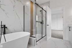 Freestanding soaking tub with matte black floor-mounted faucet, framed glass shower enclosure, and large format marble-look wall and floor tile - 