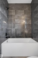 Integrated tub and shower combination featuring dark textured tile surround, matte black shower head, and matte black tub filler - 