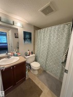 Full bathroom featuring a single vanity with wood-finish cabinetry and a neutral countertop, a toilet, and a shower area with tiled walls - 