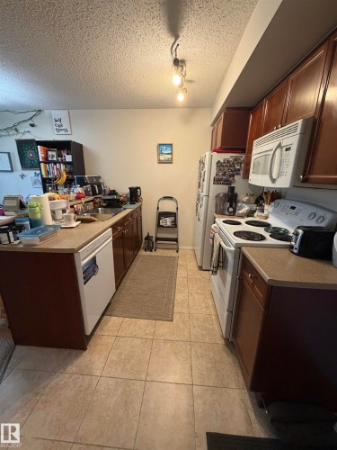 Kitchen featuring tan square floor tiles, dark wood cabinetry, light-colored countertops, and white appliances - 317 6921 199 Street, Edmonton, AB 