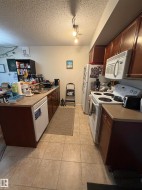 Kitchen featuring tan square floor tiles, dark wood cabinetry, light-colored countertops, and white appliances - 